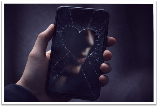 A hand holds a smartphone with a shattered screen shaped like a broken heart. Through the cracked glass, a blurred reflection of a young person’s face appears in shadow, symbolizing fractured identity and emotional struggle.
