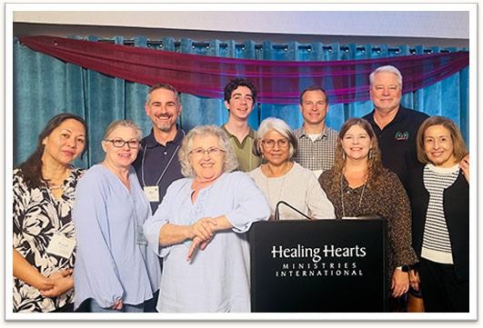 Healing Hearts leaders gathered around the Healing Hearts Ministries International podium at the 2026 National Conference