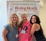 Three Healing Hearts leaders in front of a Healing Hearts banner